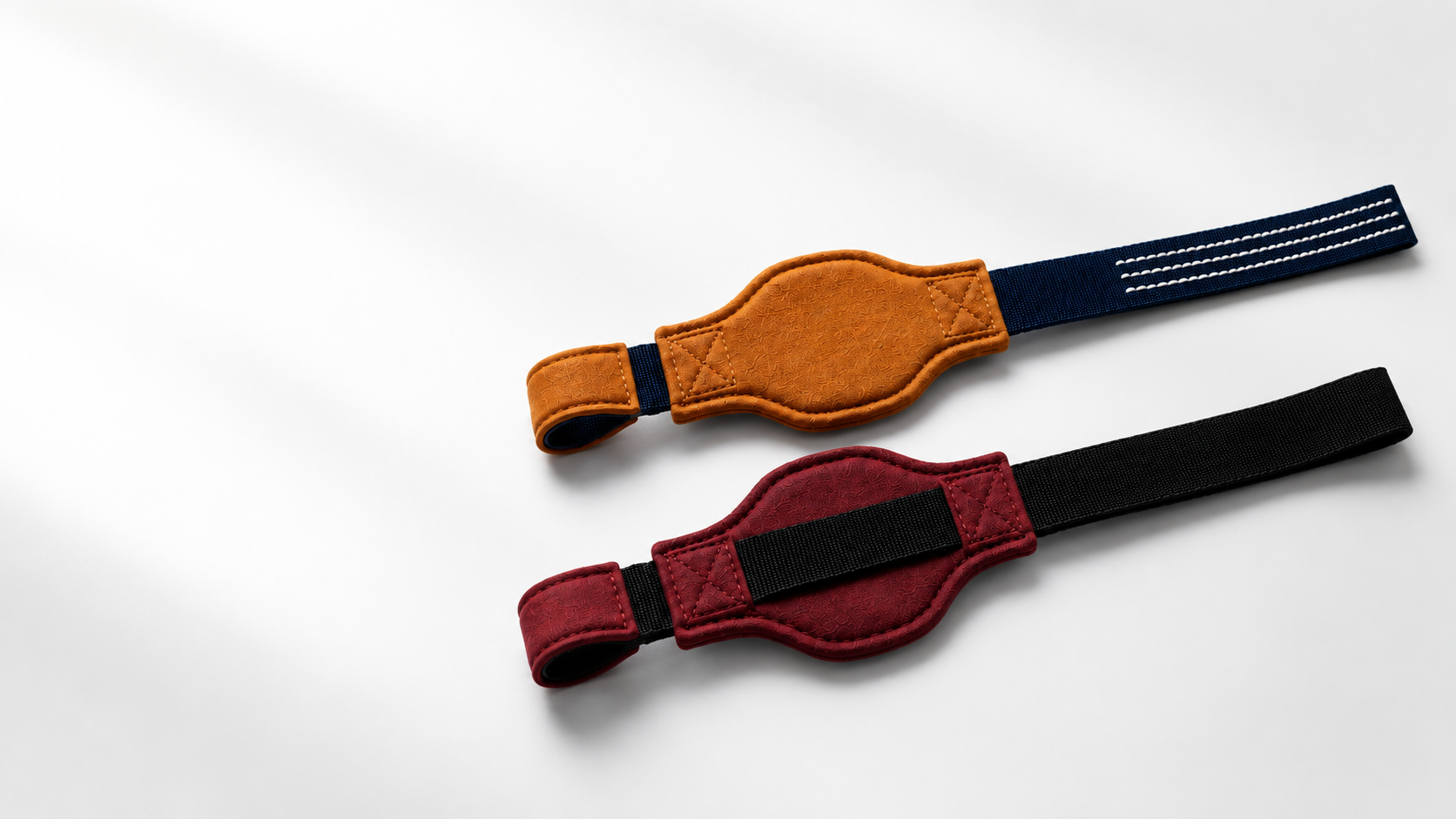Two Ælevare Loop Straps in the Caramel / Navy and Burgundy / Black colorways arranged on a light surface, showing the shaped microsuede pads, nylon webbing and woven grip threads.